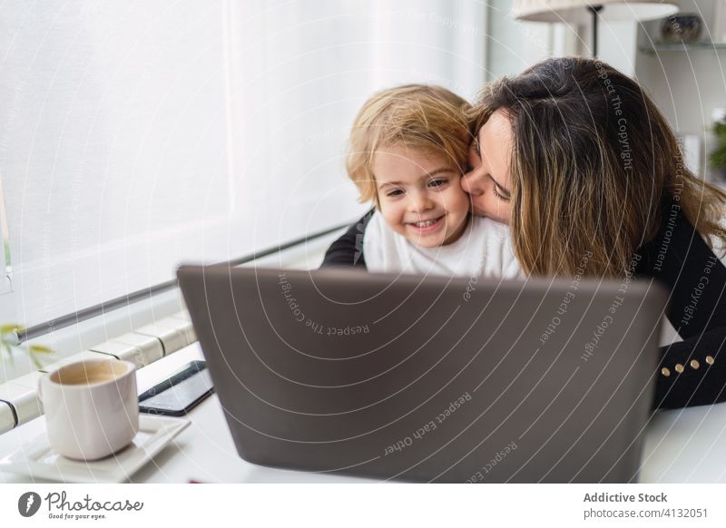 Frau mit kleinem Kind arbeitet zu Hause am Laptop Arbeit heimwärts Mutter benutzend Zusammensein Kuss online beschäftigt abgelegen neugierig Mutterschaft