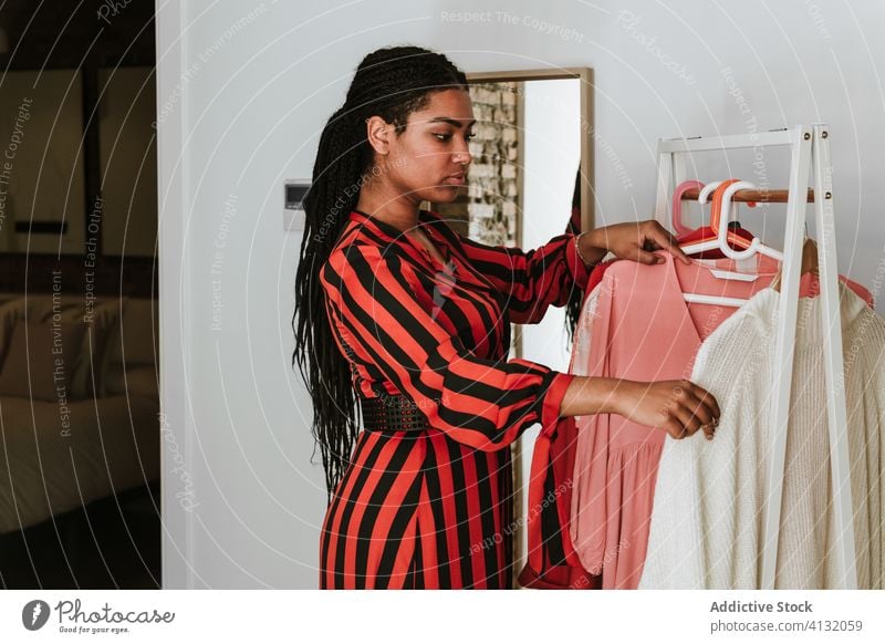 Modische schwarze Frau wählt Kleidung von der Stange Stoff heimwärts wählen Kleiderschrank Kleiderbügel Zopf Ablage Stil Mode stylisch pflücken Textil