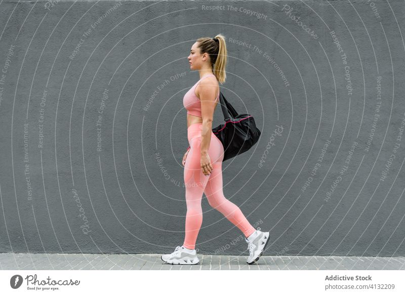 Fit Sportlerin mit Tasche zu Fuß auf Bürgersteig auf grauem Hintergrund Spaziergang Stauanlage passen Sportbekleidung Gesundheitswesen Wohlbefinden Wand