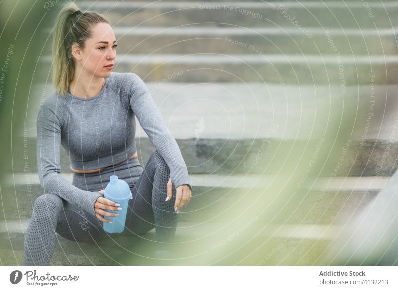 Kontemplative Sportlerin, die sich nach dem Training mit einer Flasche auf einer Treppe ausruht Athlet Pause Wasser Denken beschaulich Gesundheit ruhen