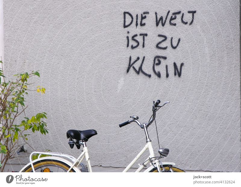 Die Welt ist zu klein Putz Wand Spray Deutsch Spruch Straßenkunst Schmiererei Fahrrad Abstellplatz Strauch Damenrad Redewendung authentisch Zufall