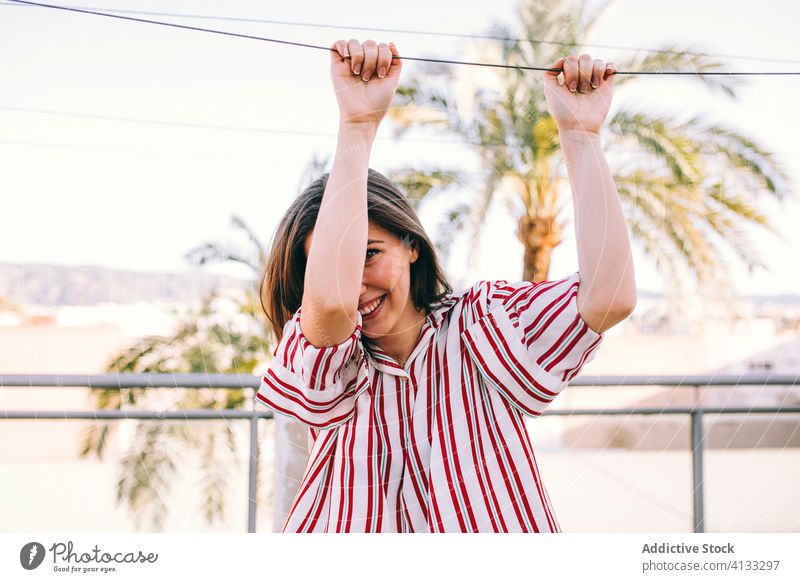 Fröhliche Frau in modischer Bluse auf dem Balkon trendy Terrasse spielerisch Stil Outfit Lächeln Spaß haben kindisch Seil Sommer positiv Bekleidung