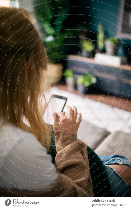 Nutzpflanzenfrau surft zu Hause auf einem Smartphone Browsen Frau heimwärts Surfen Funktelefon Wochenende unterhalten benutzend Touchscreen gemütlich Gerät