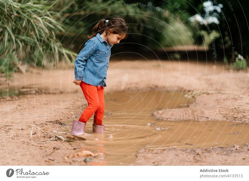 Neugieriges Mädchen spielt in einer Schlammpfütze Kind Pfütze Spaß haben Wochenende neugierig Gummi Stiefel niedlich dreckig Wasser nass bezaubernd spielen