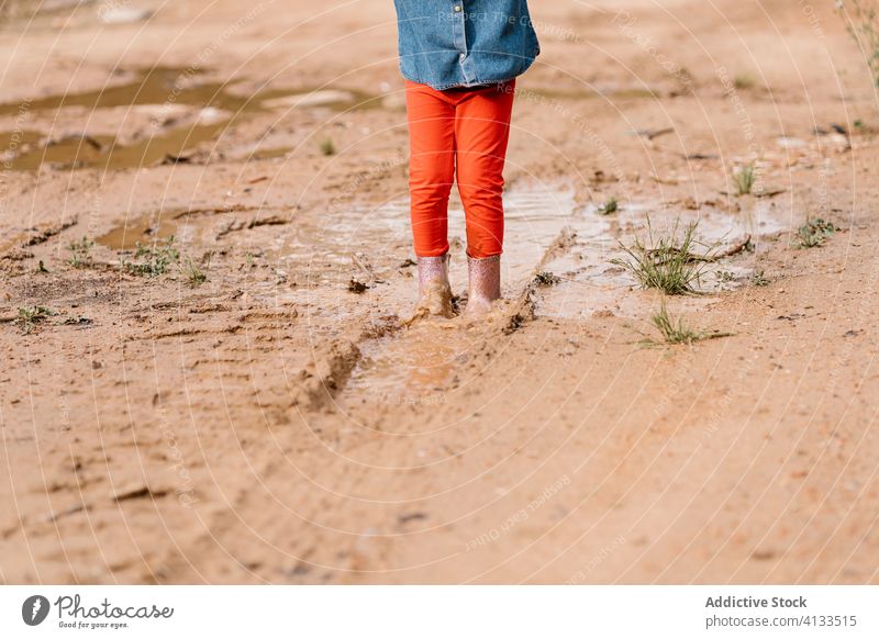 Anonymes neugieriges Mädchen spielt in einer Schlammpfütze Kind Pfütze Spaß haben Wochenende Gummi Stiefel niedlich dreckig Wasser nass bezaubernd spielen
