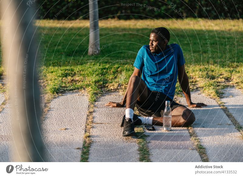 Sportlicher schwarzer Mann beim Ausruhen im Park Afrikanisch trinken Wasser Fitness hinsetzend stark Biegung Körper passen Muskel Bizeps Waffen Athlet Stärke