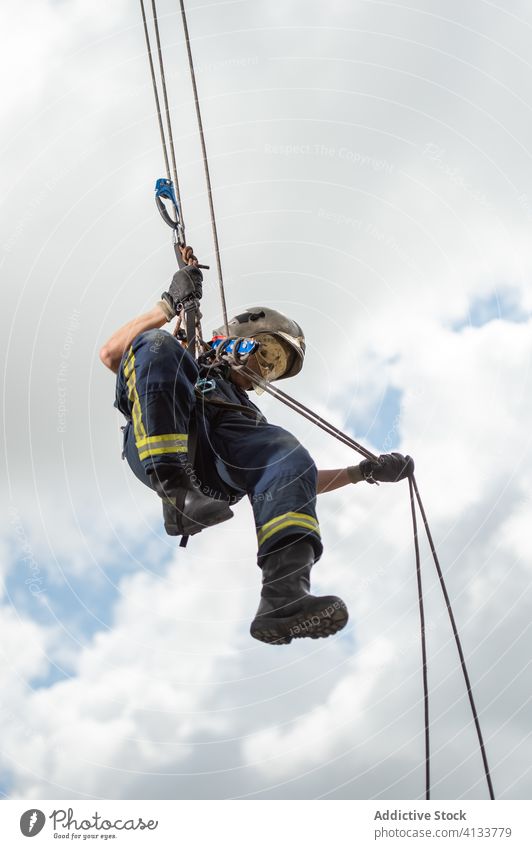 Feuerwehrmann klettert Seil gegen bewölkten Himmel herunter Training Aufstieg Gerät Mut stark Gebäude üben männlich retten komplex Uniform behüten Schutzhelm