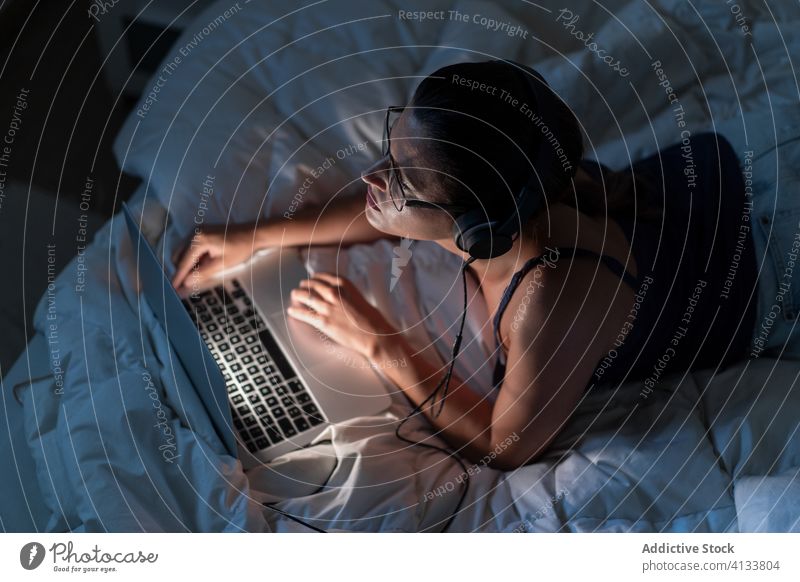 Frau hört Musik mit Kopfhörern auf dem Computer im Bett zuhören sich[Akk] entspannen genießen benutzend Gesang Browsen Decke liegend Tanktop Gerät