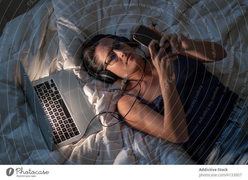 Ruhige Frau, die auf dem Bett mit Kopfhörern Musik hört zuhören sich[Akk] entspannen Smartphone genießen benutzend Gesang Browsen Decke liegend Tanktop Gerät