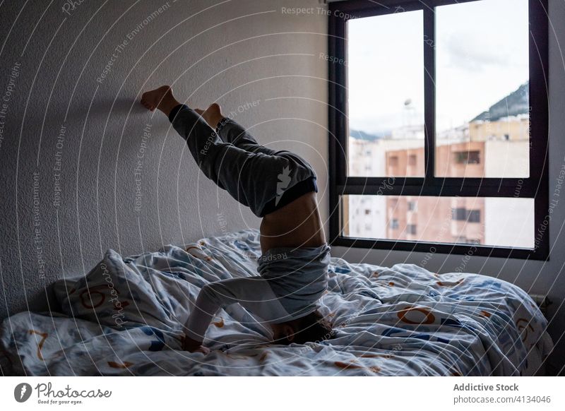 Verspielter Junge macht Kopfstand auf dem Bett zu Hause Kind niedlich spielerisch heimwärts Pyjama Spaß haben Wochenende Kindheit bezaubernd heiter Glück ruhen