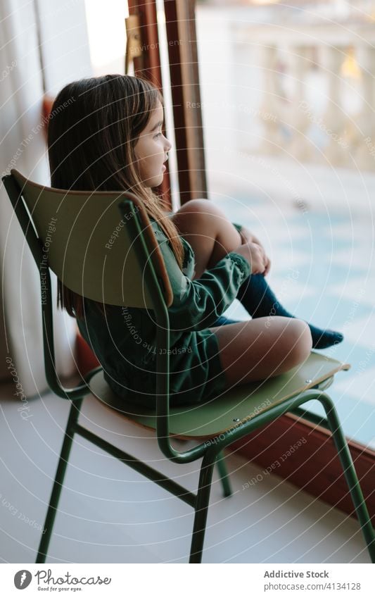 Verträumtes Mädchen sitzt auf einem Stuhl am Fenster nachdenklich Kind beobachten sich[Akk] entspannen Straße besinnlich verträumt sitzen Windstille heimwärts