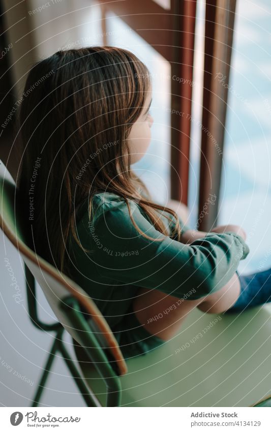 Verträumtes Mädchen sitzt auf einem Stuhl am Fenster nachdenklich Kind beobachten sich[Akk] entspannen Straße besinnlich verträumt sitzen Windstille heimwärts
