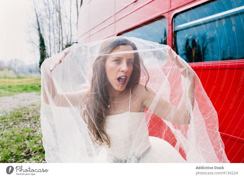 Erstaunte Braut, die ihr Gesicht mit einem Schleier bedeckt Imkerschleier Deckblatt Jungvermählter erstaunt Doppeldeckerbus Brautkleid roter Bus Hochzeit