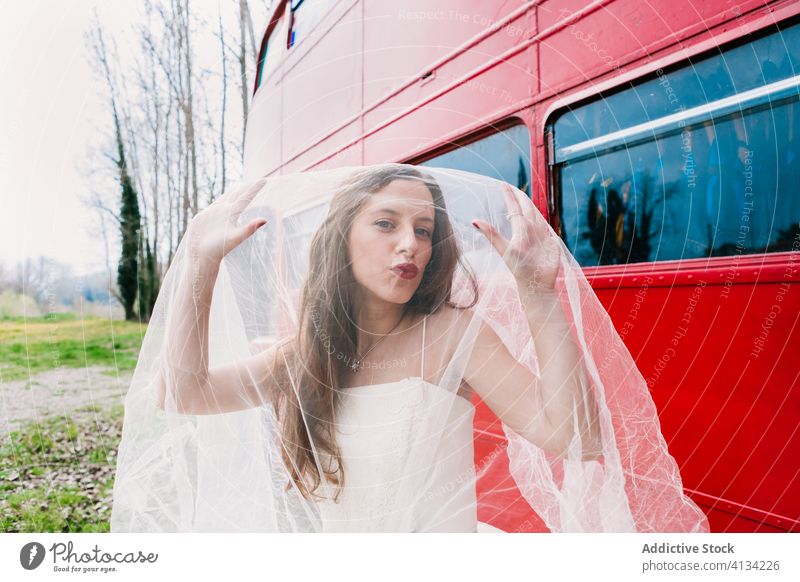 Erstaunte Braut, die ihr Gesicht mit einem Schleier bedeckt Imkerschleier Deckblatt Jungvermählter erstaunt Doppeldeckerbus Brautkleid roter Bus Hochzeit