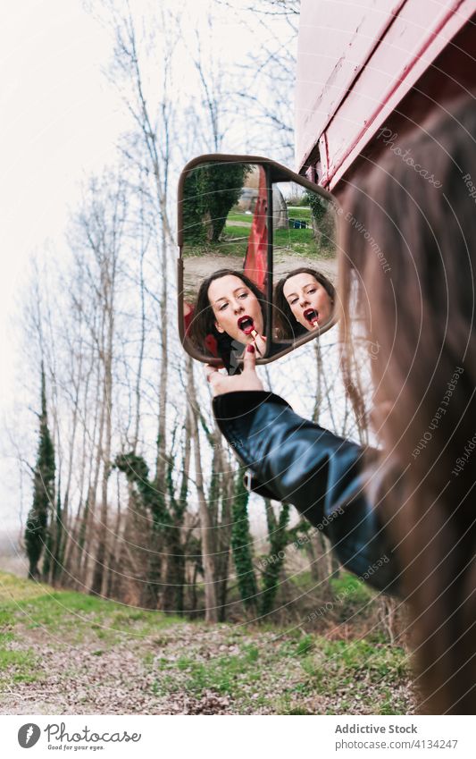 Frau trägt Lippenstift auf und schaut in den Seitenspiegel eines Busses bewerben Make-up charmant rote Lippen Lederjacke angezogen Wald Holz Natur Verkehr