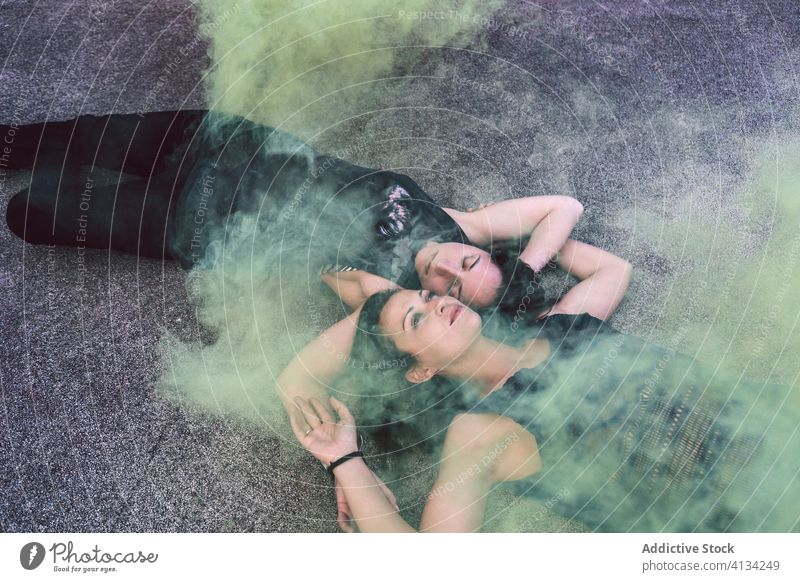 Sinnliches junges lesbisches Paar im farbigen Rauch liegend sinnlich verträumt farbiger Rauch Gelassenheit Wachtraum gelb Asphalt Boden Frauen Lügen