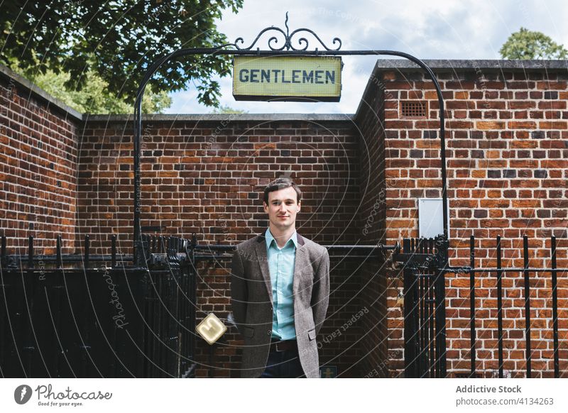 Zufriedener Mann in eleganter Jacke auf der Straße stilvoll Kavalier Lächeln Schild Gebäude Baustein wc Öffentlich männlich London England