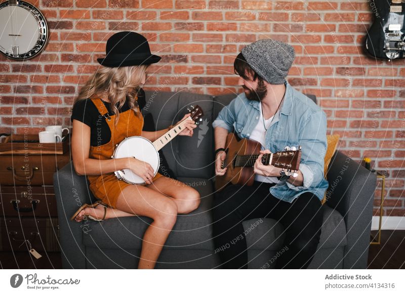Fröhliches Paar, das auf dem Sofa sitzend Gitarre und Banjo spielt spielen banjo Musik Freizeit Duett Partnerschaft Freundschaft Zusammensein Beine gekreuzt