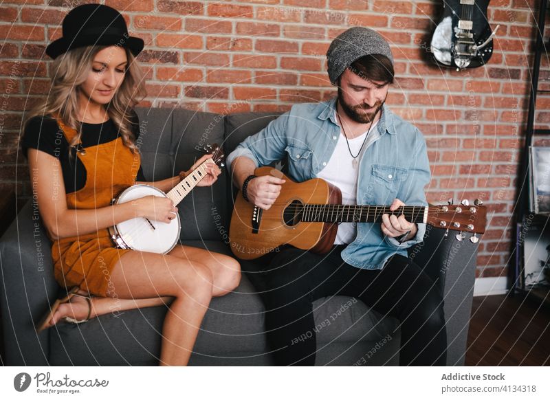 Fröhliches Paar, das auf dem Sofa sitzend Gitarre und Banjo spielt spielen banjo Musik Freizeit Duett Partnerschaft Freundschaft Zusammensein Beine gekreuzt