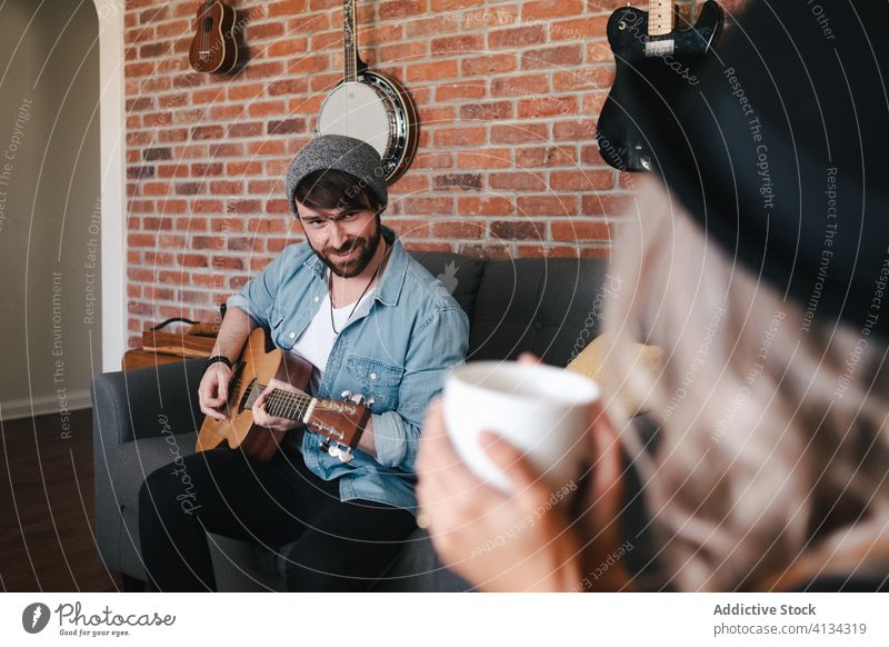 Musiker spielt Gitarre und sitzt mit seiner Freundin auf dem Sofa zu Hause Paar spielen Freizeit Komfort Wohnzimmer Freundschaft Zusammensein Partnerschaft