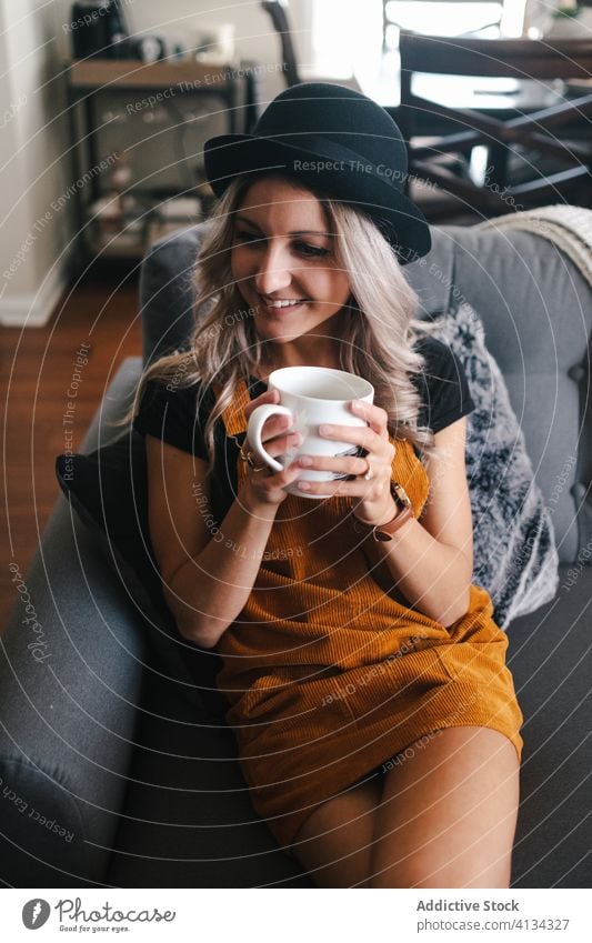 Glückliche junge Frau mit einer Tasse Kaffee auf einem Stuhl sitzend Lächeln heimwärts Stil Komfort selbstbewusst ruhen angenehm Windstille schlank ruhig heiter