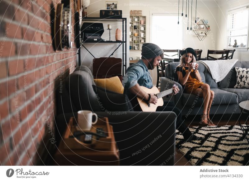 Musiker spielt Gitarre und sitzt mit seiner Freundin auf dem Sofa zu Hause Paar spielen Freizeit Komfort Wohnzimmer Freundschaft Zusammensein Partnerschaft