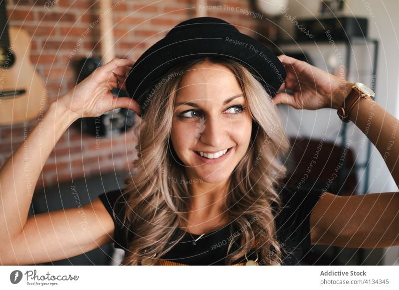 Positive Frau mit schwarzem Hut in Wohnung Hipster Glück Zahnfarbenes Lächeln Freizeit schlank Loft Design heimwärts Sofa froh positiv charismatisch schlanke