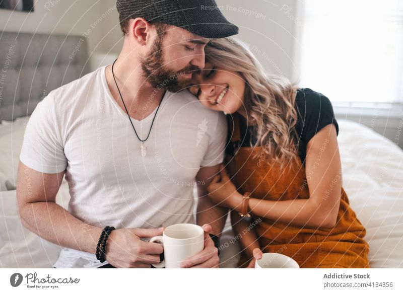 Glückliches Paar umarmt sich im Schlafzimmer beim Kaffeetrinken Umarmen Hipster Bett Komfort Becher Tasse Partnerschaft Morgen Harmonie Liebe Romantik Zuneigung