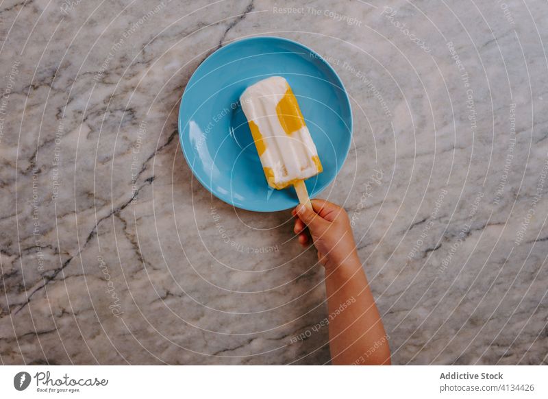 Anonymes Kind schnappt sich einen selbstgemachten Eislutscher auf einem Teller Stieleis kleben Kies Speiseeis lecker Sommer Leckerbissen Dessert süß frisch