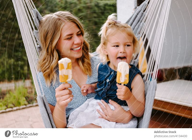 Glückliches kleines Mädchen und Frau mit hausgemachten Eis am Stiel Mutter Tochter Umarmung Stieleis selbstgemacht Kies genießen heiter Sommer Terrasse Lächeln