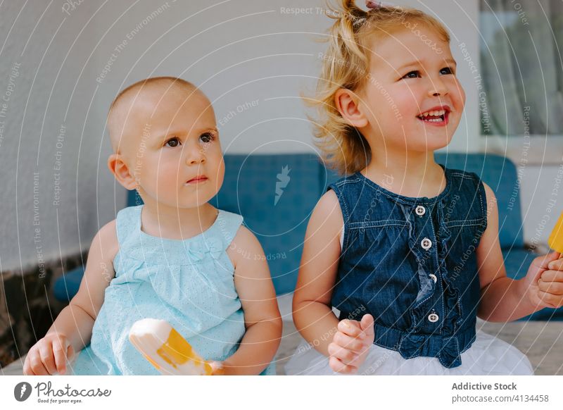 Zufriedene Schwestern essen selbstgemachte Eislutscher auf der Terrasse Stieleis Kies Mädchen Kind Zusammensein lecker Kleinkind wenig süß niedlich Hof