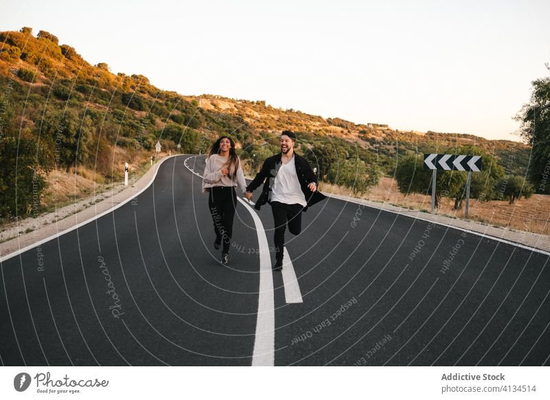 Unbekümmertes gemischtrassiges Paar läuft die Straße entlang Freiheit sorgenfrei laufen Berge u. Gebirge Sonnenuntergang Zusammensein Partnerschaft