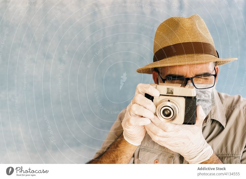 Älterer Mann mit Schutzhandschuhen, der mit einer alten Kamera fotografiert Fotoapparat retro Mundschutz behüten Fotokamera professionell Atelier altehrwürdig