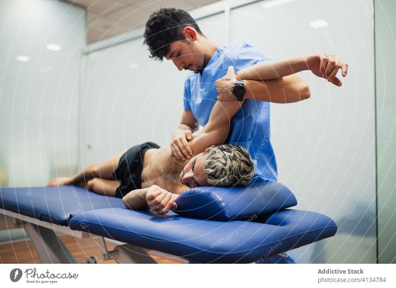 Orthopäde mit Maske, der den Arm eines Sportlers bei einer medizinischen Untersuchung streckt geduldig Wiederherstellung untersuchen Arme strecken professionell