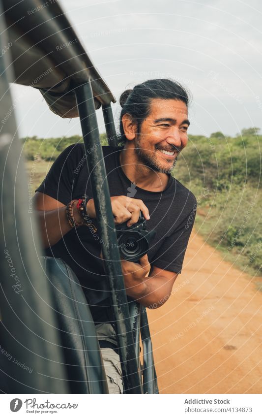 Ethnischer männlicher Fotograf, der aus dem Auto heraus ein Bild mit der Kamera aufnimmt fotografieren Safari Mann Landschaft reisen Tierwelt Natur Fotoapparat