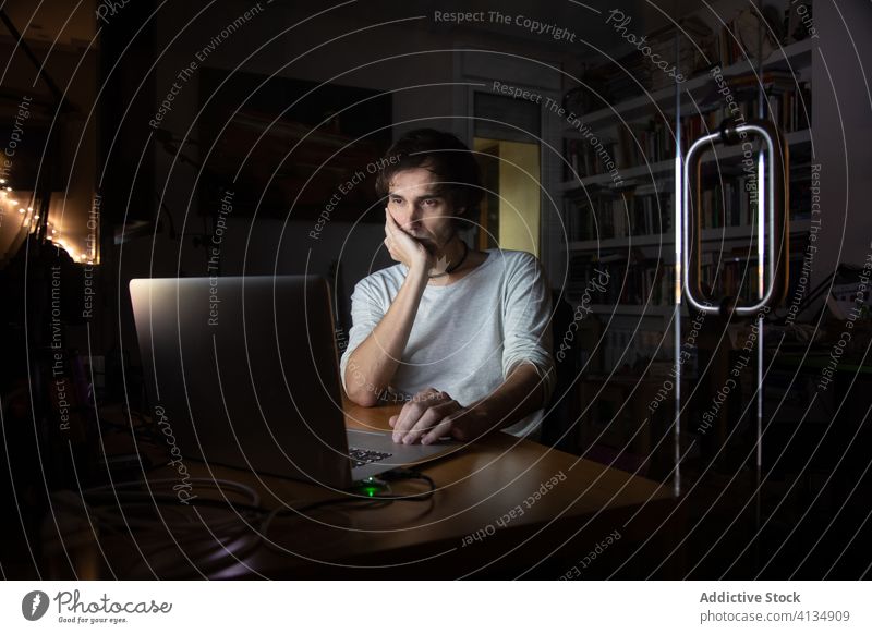 Ernster Mann arbeitet nachts aus der Ferne zu Hause Arbeit heimwärts Laptop Smartphone benutzend Anruf Nacht dunkel Arbeitsplatz abgelegen Entfernung