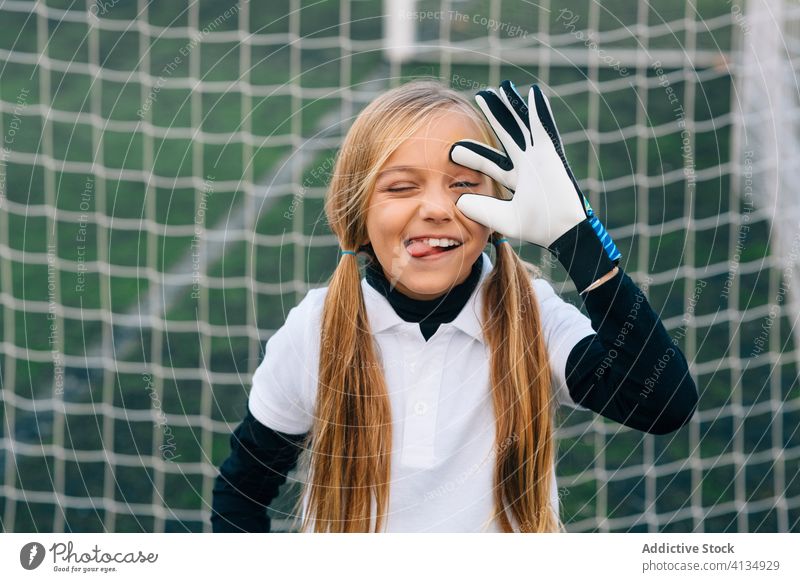 Fröhliches Mädchen im Teenageralter, das als Torwart auf dem Fußballplatz im Sportstadion seinen Rivalen ärgert Ball Handschuh Gesicht machen Training