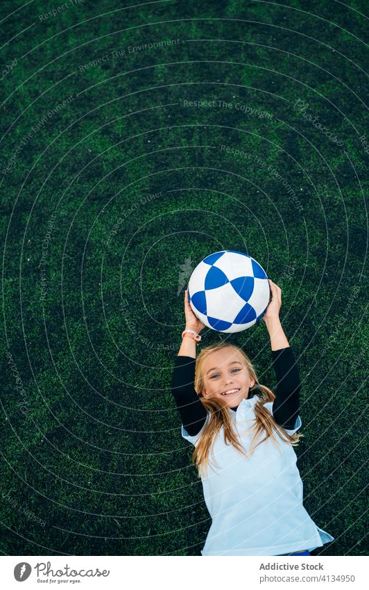 Zufriedene junge Spielerin wirft den Ball hoch, während sie auf dem Fußballfeld liegt Mädchen werfen Spaß haben ruhen Feld Kind Stadion sich[Akk] entspannen