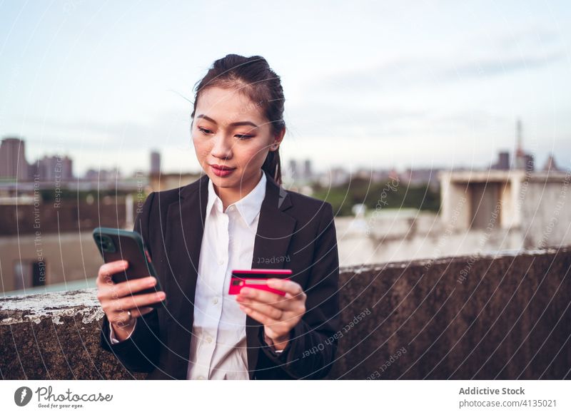 Beschäftigte ethnische Frau mit Kreditkarte und Smartphone beschäftigt ernst Problematik benutzend formal jung asiatisch Geschäftsfrau Kunde Dachterrasse