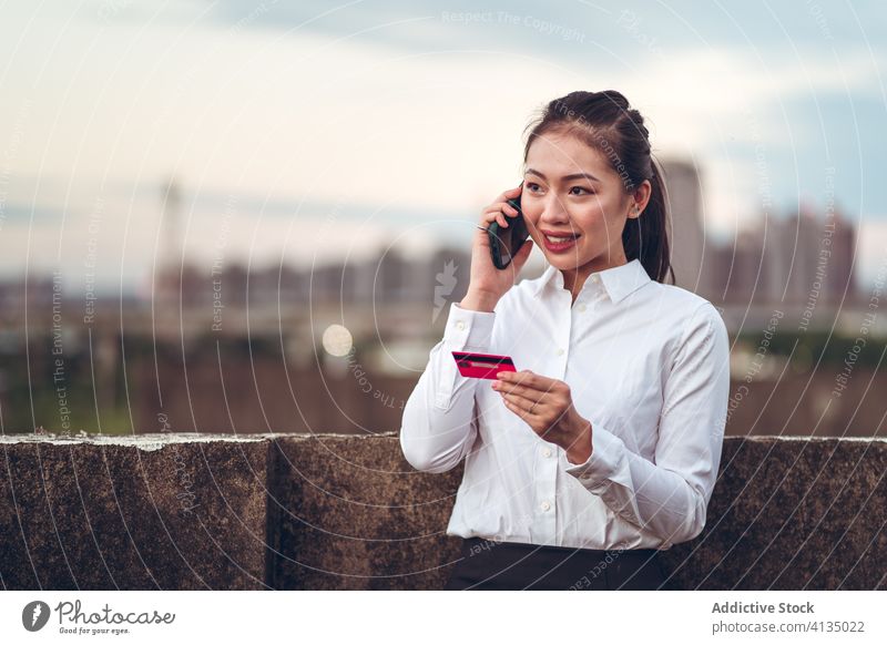 Vielbeschäftigte ethnische Frau mit Kreditkarte telefoniert Telefonanruf ernst reden Smartphone Problematik diskutieren formal jung asiatisch Geschäftsfrau