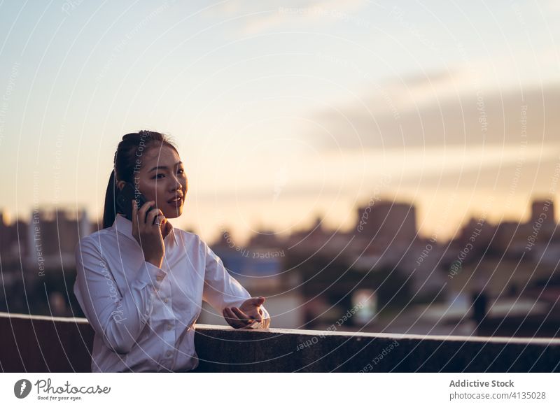 Beschäftigte Frau, die mit ihrem Smartphone spricht Arbeit benutzend reden Geschäftsfrau formal Dachterrasse Gerät Apparatur Business asiatisch jung Internet