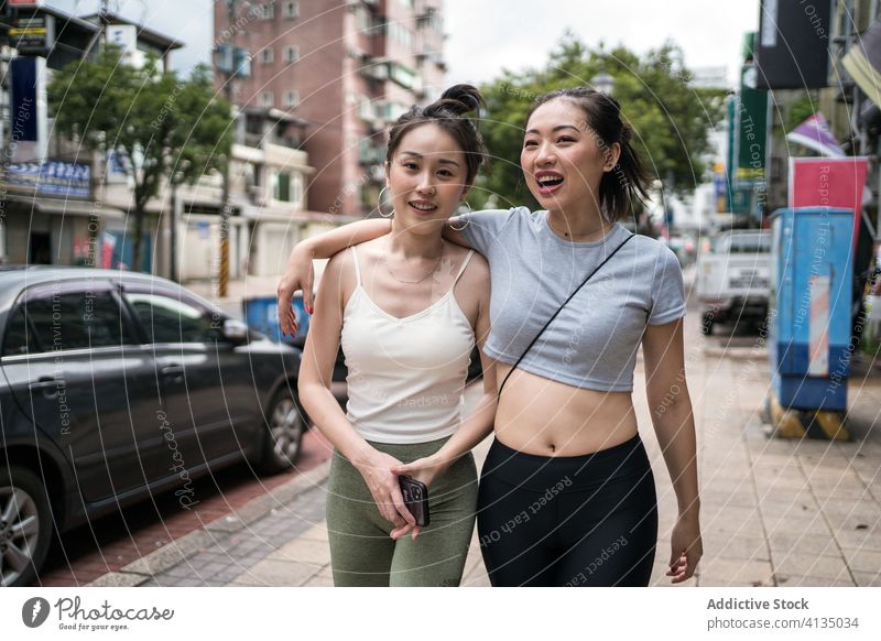 Fröhliche ethnische Freundinnen auf der Straße Spaziergang Umarmung Glück heiter Schulter lässig schlank Umarmen Taipeh Taiwan Zusammensein schlendern Lifestyle