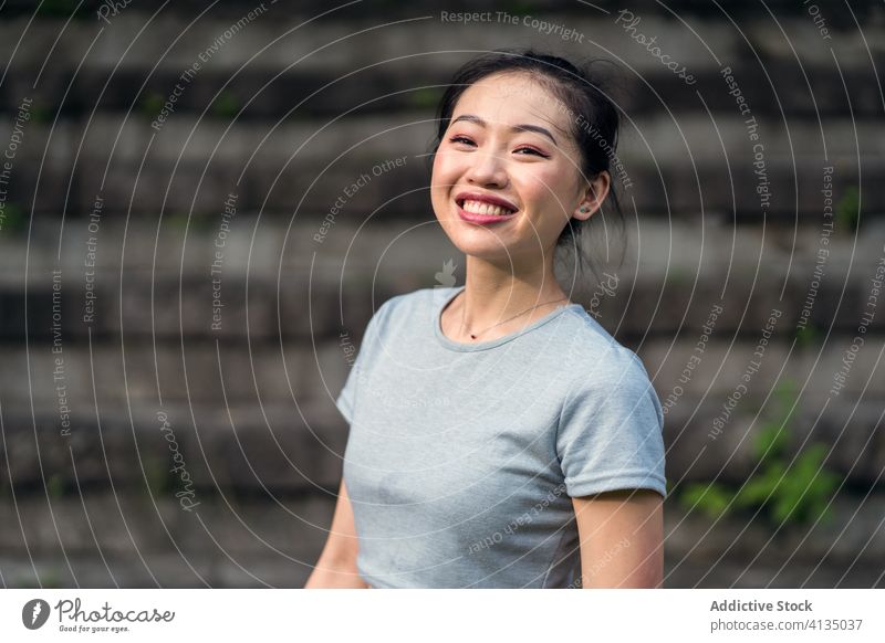 Positive ethnische Frau, die auf einer schäbigen Treppe im Park sitzt Treppenhaus ruhen Glück positiv Zahnfarbenes Lächeln lässig sportlich Gelassenheit passen