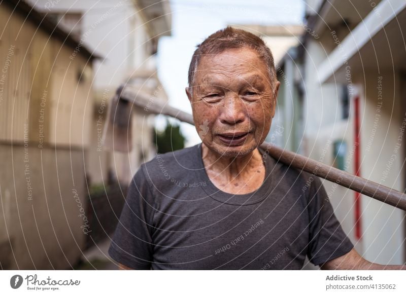 Älterer ethnischer Bauer mit Hacke auf der Straße im Township Landwirt Senior Mann Gärtner Stadt Vorschein Lächeln Porträt Orientalisch Werkzeug urban Taiwan