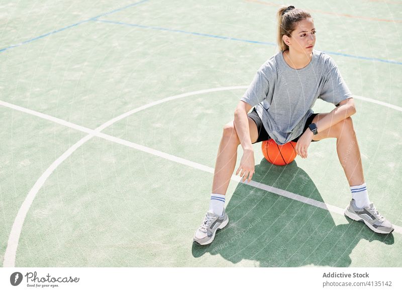 Basketballspielerin auf dem Sportplatz sitzend Frau Ball Übung Aufwärmen Sportpark Training vorbereiten Spieler Gericht Aktivität Lifestyle Wohlbefinden jung