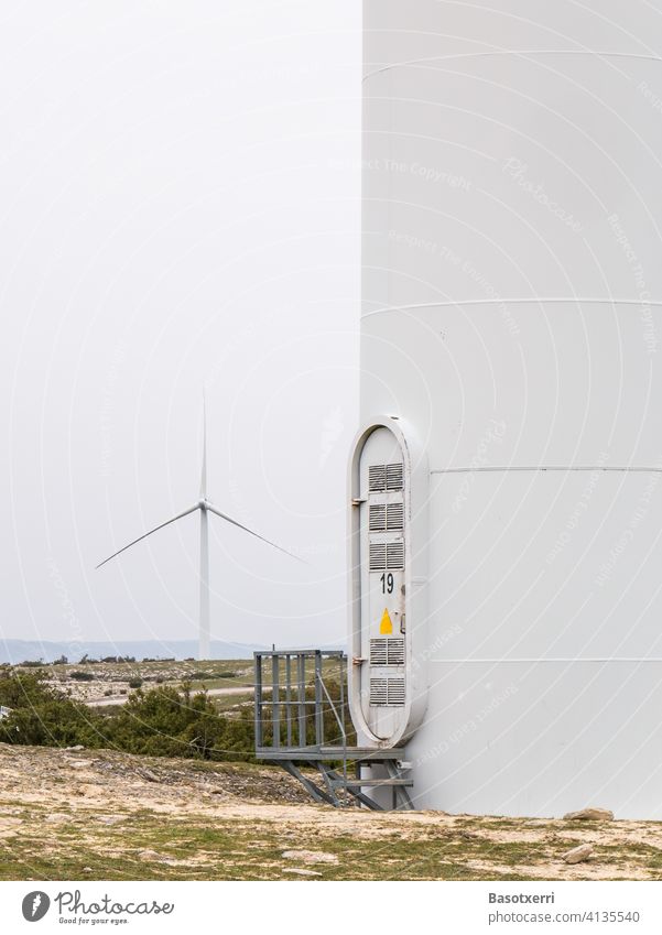 Detailaufnahme eines Windparks im nordspanischen Gebirge - Turm mit Eingang/Aufstieg, eine weitere Windkraftanlage im Hintergrund 19 weiß Energiewirtschaft