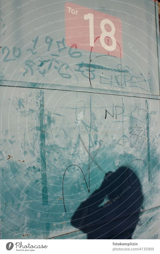 Schatten einer fotografierenden Frau an einer Torwand Wand 18 Zahl Graffiti Schmiererei Schriftzeichen ausgeschlossen Stillstand Geschmackssache Fassade Gebäude
