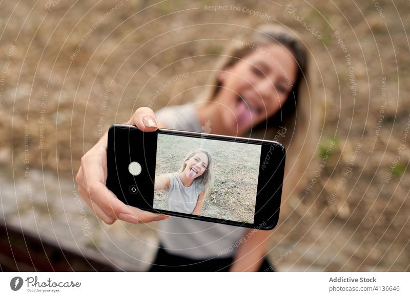 Fröhliche Frau macht Selfie mit Smartphone heiter Gesicht machen Zunge zeigen Spaß haben jung Straße spielerisch Glück Foto Gerät Apparatur Bildschirm Lifestyle