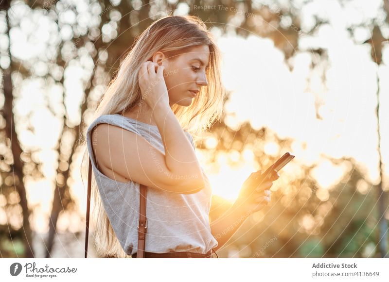 Glückliche Frau mit Smartphone im Park stehend heiter benutzend genießen Browsen jung trendy Lifestyle Apparatur Gerät ruhen Kälte positiv soziale Netzwerke