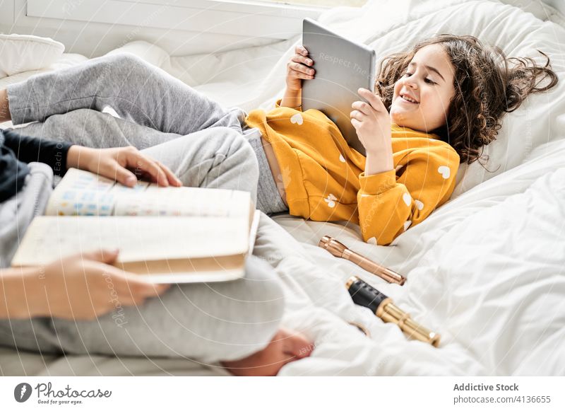 Ruhige Geschwister, die sich auf dem Bett mit Buch und Gerät entspannen Geschwisterkind sich[Akk] entspannen Tablette Mädchen Junge lesen zuschauen benutzend